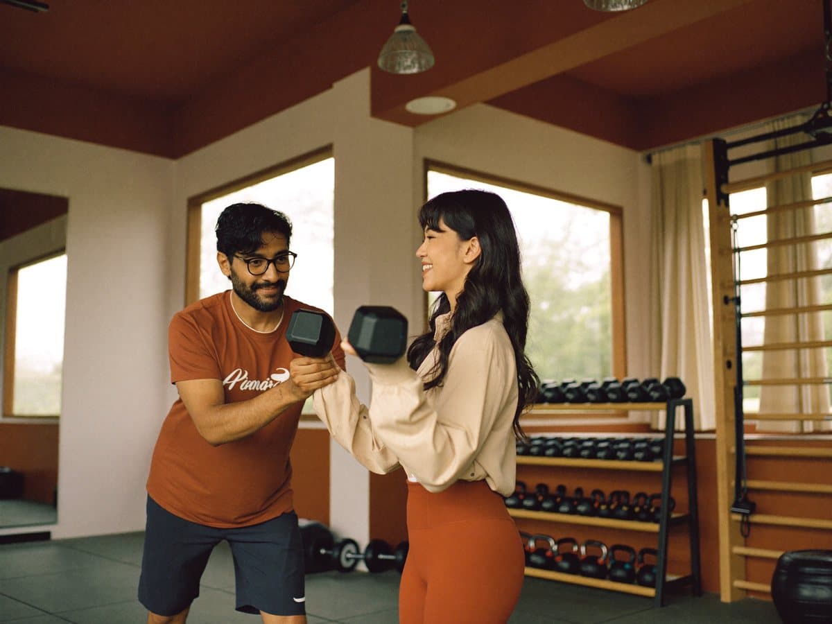 Coach personal training mendampingi member angkat beban di gym